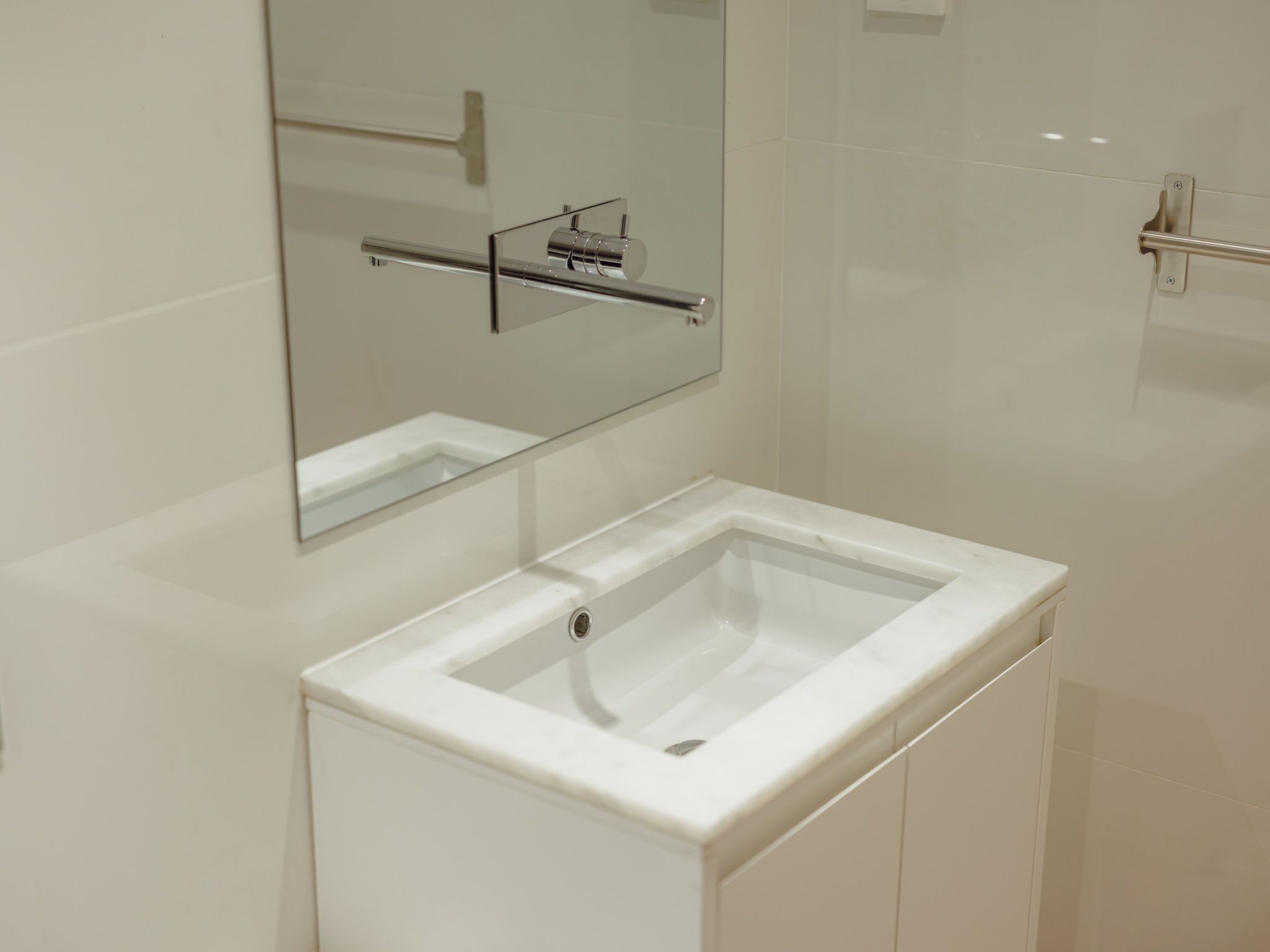 Een badkamer met een witte wastafel, een spiegel en een handdoekhouder.