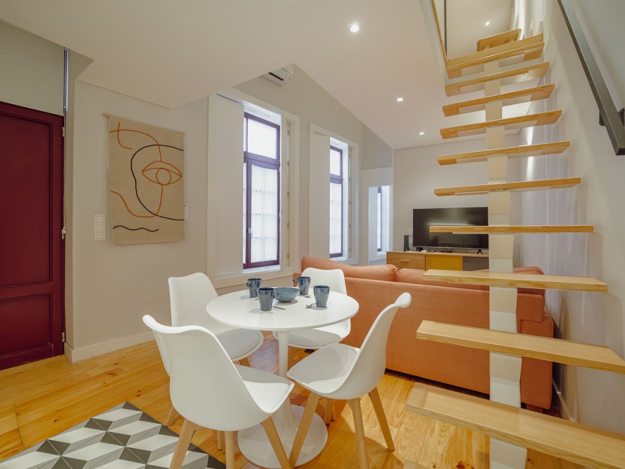 A modern living space with a dining area, sofa, TV, and a staircase.