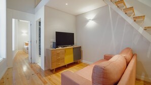 Ein modernes Wohnzimmer mit einer Couch, einem Fernseher auf einem Holzschrank und einer Treppe.