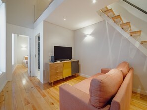 Uma sala de estar moderna com um sofá, uma televisão sobre um móvel de madeira, e uma escada.
