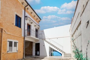 Eine enge Straße mit Gebäuden an beiden Seiten, eine Treppe, die zu einem Balkon führt, und ein klarer Himmel.
