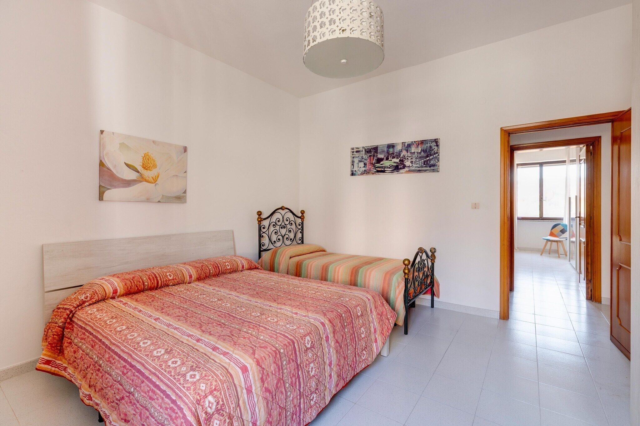 A bedroom with a large bed, two smaller beds, a ceiling light fixture, and artwork on the walls.