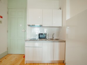 A compact kitchen with white cabinets, a microwave, a sink, and a stainless steel range hood. - Apartment  by Interhome (Porto)