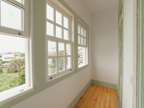 A narrow hallway with three windows, wooden flooring, and a view of buildings and greenery outside. - Apartment  by Interhome (Porto)