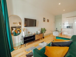 A modern living room with a flat-screen TV, a round mirror, a sofa with cushions, a coffee table, and a small kitchen area with a microwave. - Apartment  by Interhome (Porto)