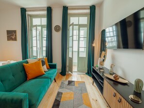 A modern living room with a teal sofa, a wooden floor, and a large TV on the wall. - Apartment  by Interhome (Porto)