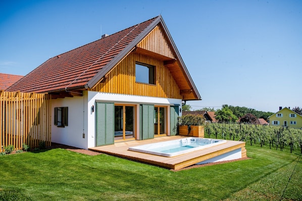 Una casa de madera de dos pisos con techo inclinado, piscina y viñedo al fondo.