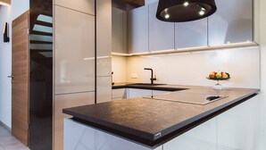 A modern kitchen with a central island, a black countertop, and a fruit bowl on the island. - Klöchberg R&L APP Sunrise - Gelber Muskateller (Klöch)