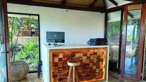Una recepción con un escritorio, un taburete de madera y vistas a zonas verdes al exterior.