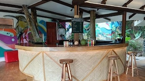 Una zona de bar con mostrador de madera, taburetes, carta de bebidas y un mural de fondo.