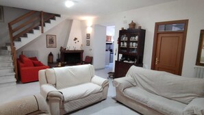 Una sala de estar con una escalera, dos sofás, un sillón rojo, una chimenea y un aparador de madera.
