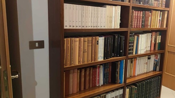Una estantería llena de libros, una puerta de madera y un interruptor de luz en la pared.
