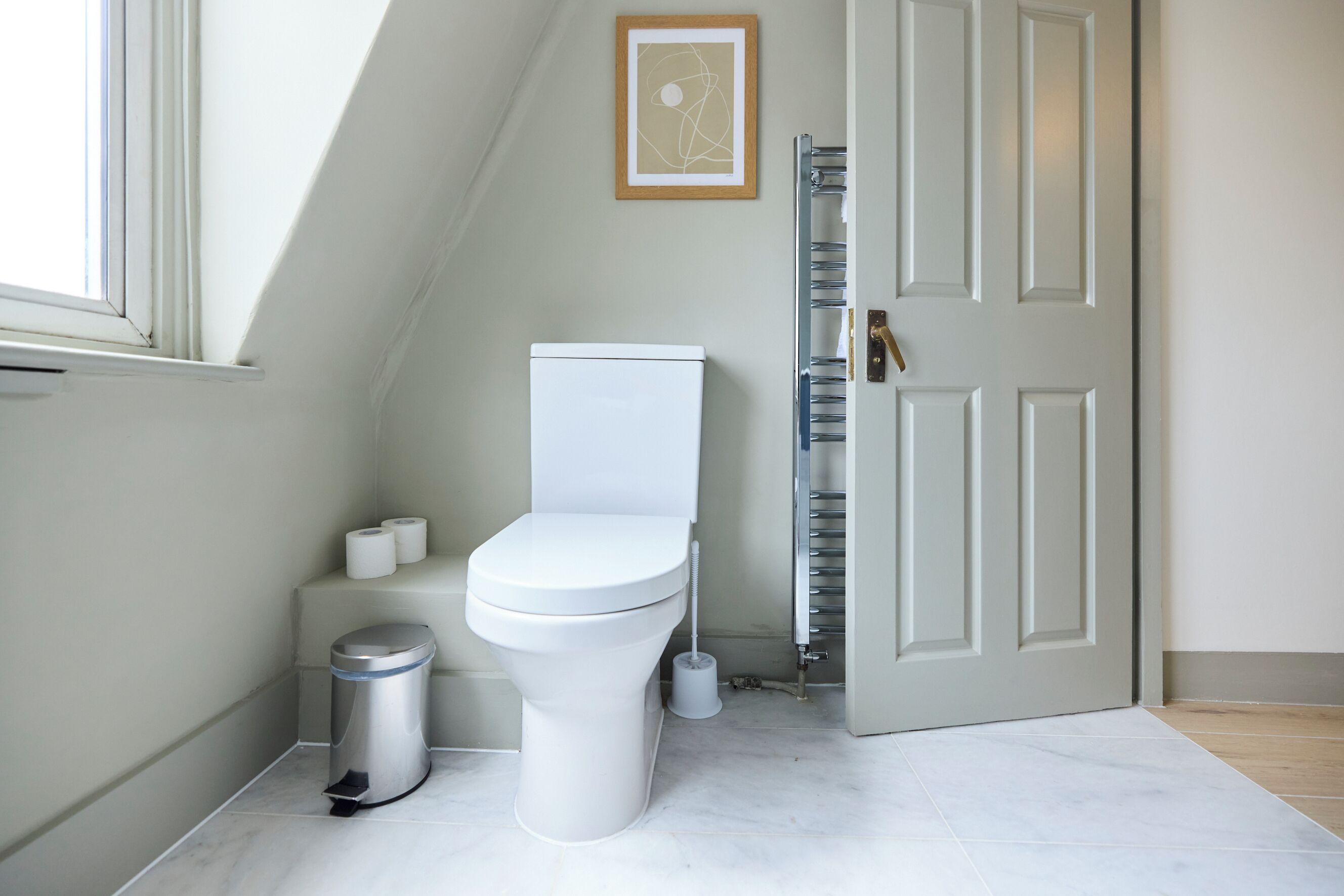 Une salle de bain moderne avec des toilettes, une poubelle, une brosse pour les toilettes et un tableau encadré au mur.