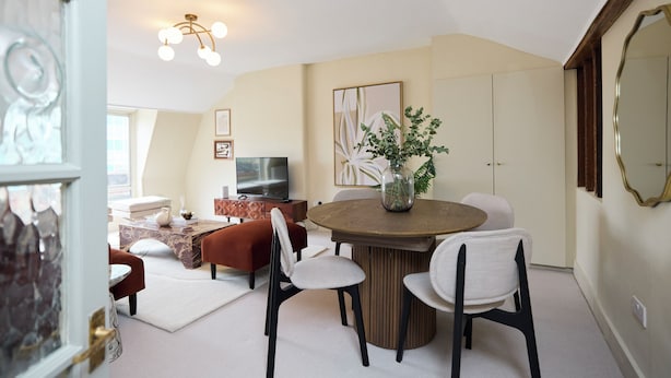 Un salon moderne avec une table ronde en bois, des chaises blanches, un téléviseur et un grand miroir.
