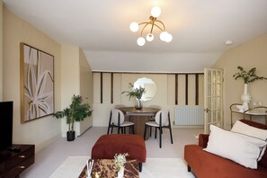 A modern living room with a television, a dining table with chairs, a sofa, a coffee table, and a large mirror. - The Fourth Above Dorset Square (London)