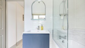 Une salle de bain avec un lavabo blanc, un meuble bleu et une douche à parois de verre.
