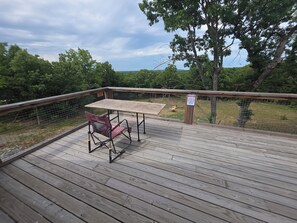 Eine Holzterrasse mit Tisch und Stuhl, umgeben von einem Geländer und einem Warnschild.