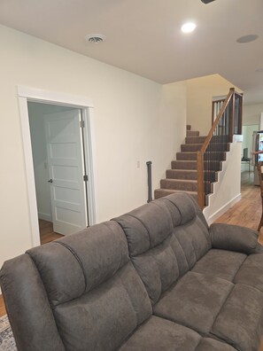 Ein Wohnzimmer mit grauem Sofa, einer Treppe und einer weißen Tür.