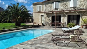 Un bâtiment en pierre doté d’une piscine, de chaises longues extérieures et d’un palmier.