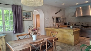 Une cuisine avec une table à manger en bois, des chaises, un luminaire suspendu et une cuisinière.