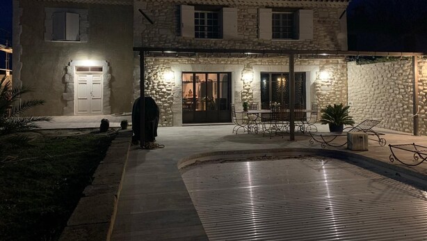 Un bâtiment en pierre doté d’un patio couvert, d’un espace repas avec des chaises en métal et d’une porte à panneaux de verre.