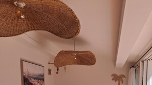 A living room with a sofa, a wooden coffee table, a hanging light fixture, a wall-mounted picture, and a window with curtains. - T2 air-conditioned, Wifi broadband, garden level, Gigaro beach and paths 500m away (La Croix-Valmer)