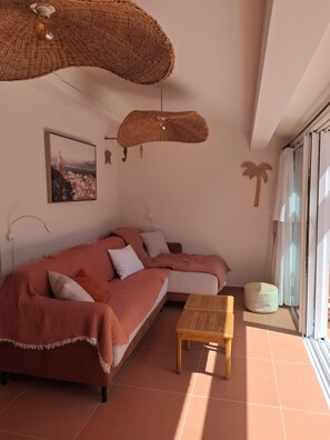 Ein Wohnzimmer mit Sofa, einem Holztisch, einer Pendelleuchte, einem Wandbild und einem Fenster mit Vorhängen.