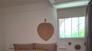 A bedroom with a bed, a small wooden stool, a wall-mounted light, and a window with curtains. - T2 air-conditioned, Wifi broadband, garden level, Gigaro beach and paths 500m away (La Croix-Valmer)