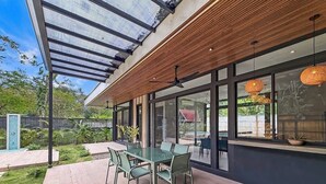 A modern outdoor dining area with a glass table and chairs, a wooden ceiling, and large windows. - A Secluded Modern Villa with Private Pool, Jungle Oasis Bathtub & Beach Access (puerto viejo de talamanca)