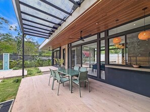 A modern outdoor dining area with a glass table and chairs, a wooden ceiling, and large windows. - A Secluded Modern Villa with Private Pool, Jungle Oasis Bathtub & Beach Access (puerto viejo de talamanca)