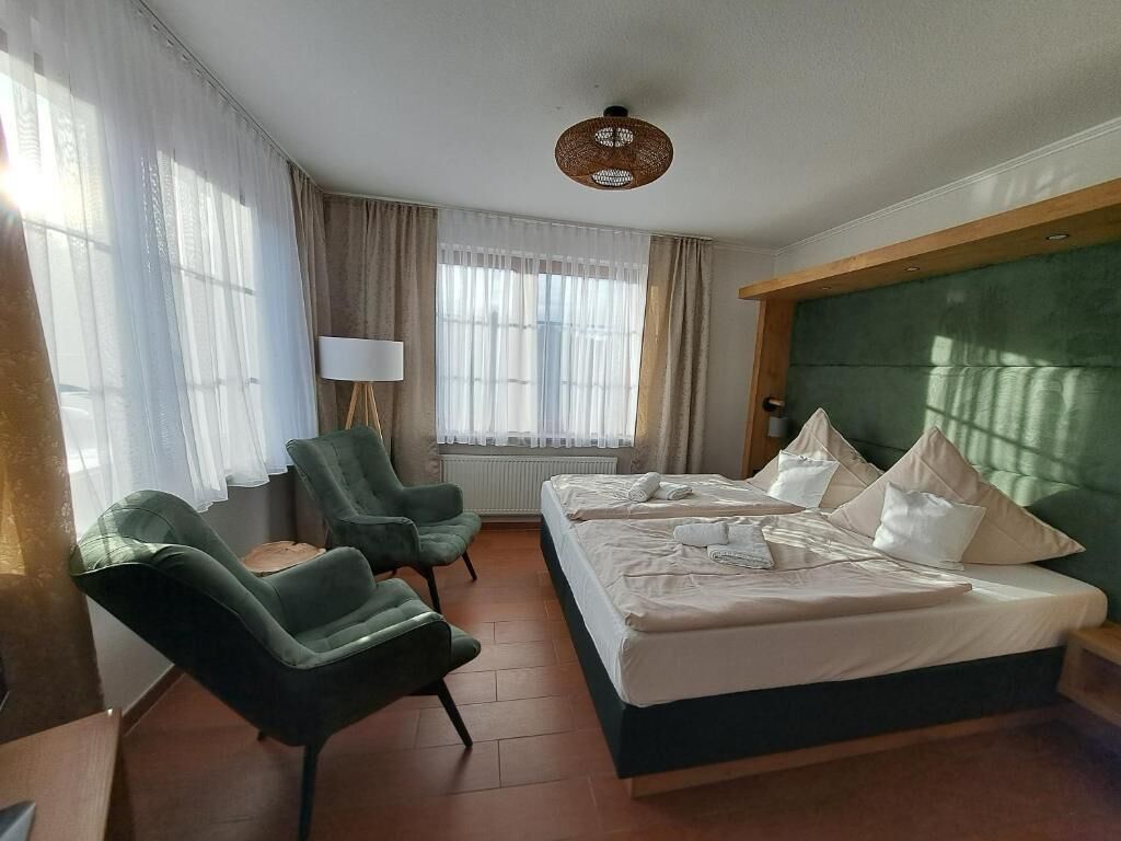 A hotel room with two beds, a sitting area with chairs, a lamp, and a large window with curtains.