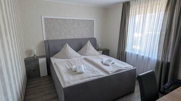A hotel room with a large bed, bedside tables, a desk, and a window with curtains.