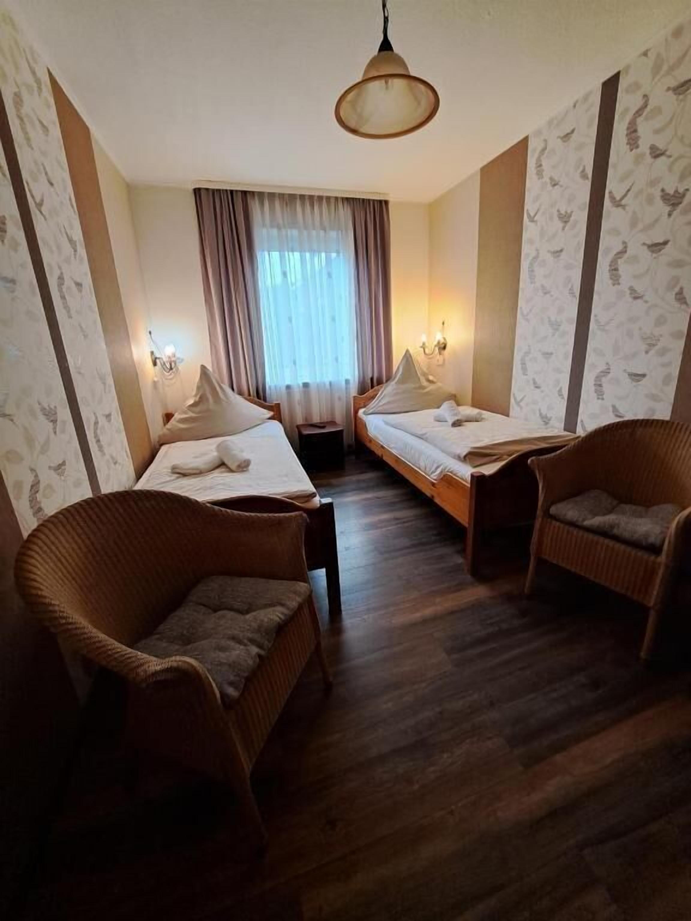 A hotel room with two single beds, a sofa, two armchairs, a small table, and a ceiling light.