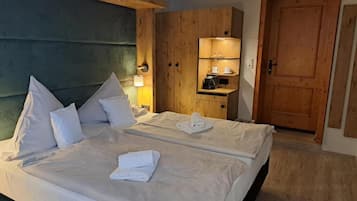 A double bed with white linens, a wooden wardrobe, a bedside table with a lamp, and a door to the right.