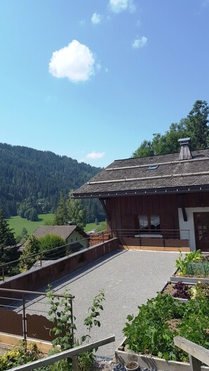 Ein Holzhaus mit geneigtem Dach, einem Balkon und Blick auf ein grünes Tal und bewaldete Hügel.