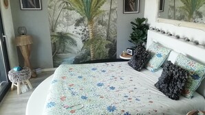 A bedroom with a bed, floral bedspread, a wall mural, a small stool, and a nightstand with a lamp. - Spacious architect-designed villa in quiet location with tourist access PÉZENAS.BEZIERS.SETE.AGDE (Laurens)