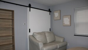 Et værelse med en beige lædersofa, et lille rundt bord, en træreol og en skydedør.