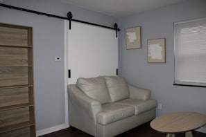 Ein Zimmer mit einem beigefarbenen Ledersofa, einem kleinen runden Tisch, einer Holzregaleinheit und einer Schiebetür.
