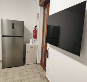 A kitchen with a stainless steel refrigerator, a small white cabinet, a fire extinguisher, and a large flat-screen TV mounted on the wall. - Salento abode a stone's throw from the sea - independence and relaxation in Baia Verde (Baia Verde)