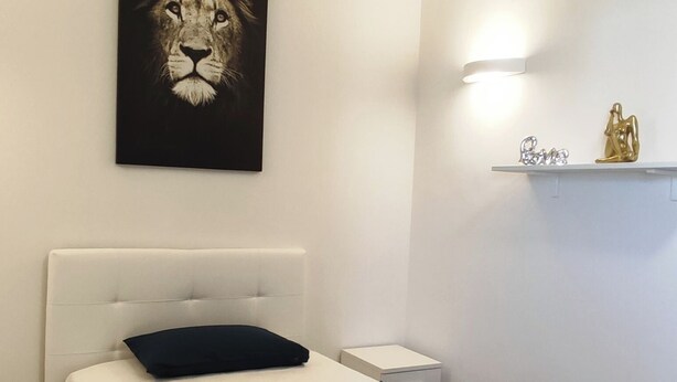 Hotelkamer met een bed, een kunstwerk van een leeuwenkop aan de muur, een nachtkastje, en een plank met decoratieve objecten.