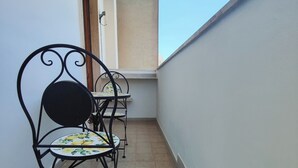 Een smal balkon met een betegelde vloer, een metalen stoel met een bloemenkussen en een klein tafeltje.