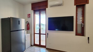 Een keuken met een koelkast, een klein aanrecht, een brandblusser en een grote flatscreen-televisie aan de muur.