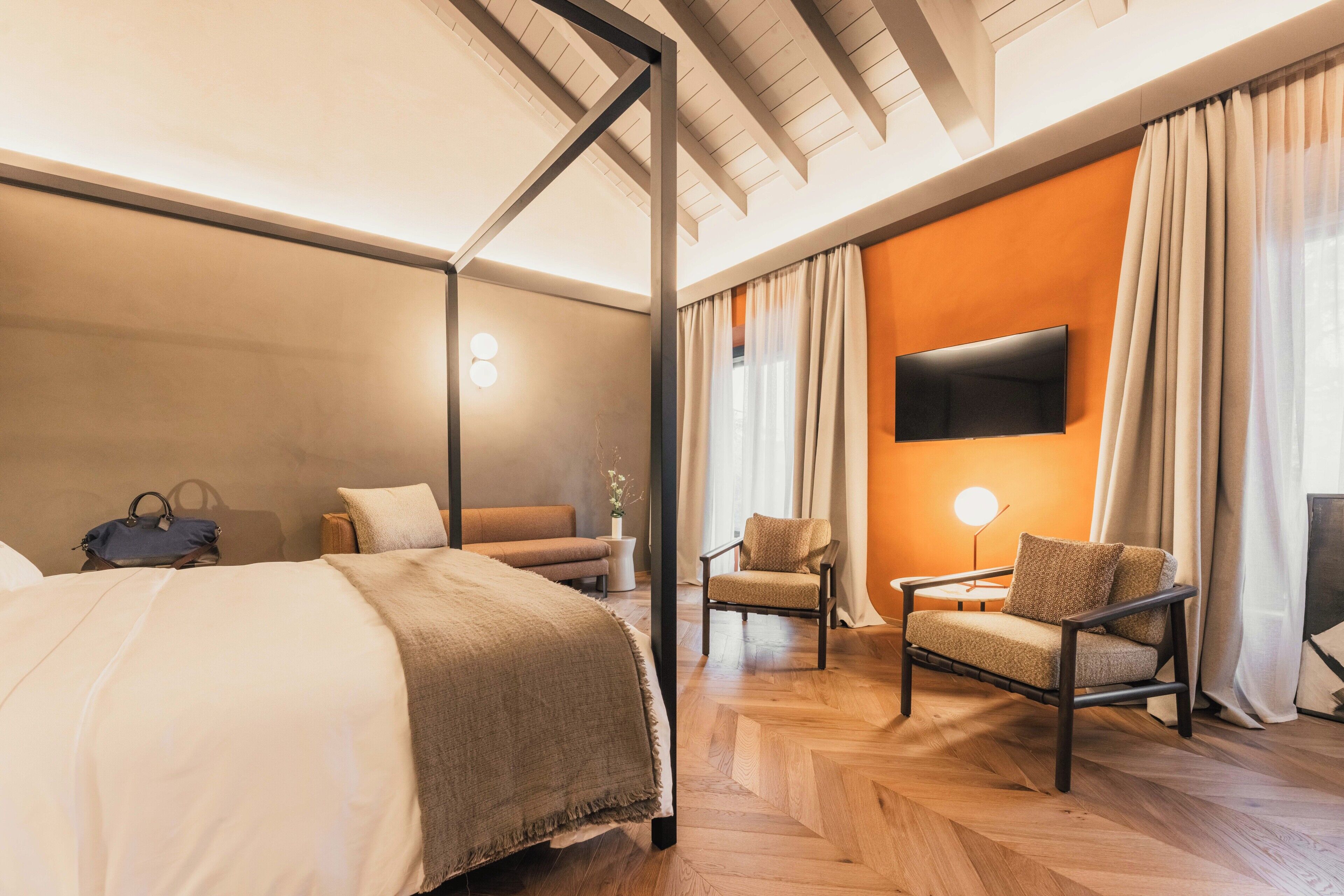 A hotel room with a bed, a sofa, a chair, a TV, and a lamp.