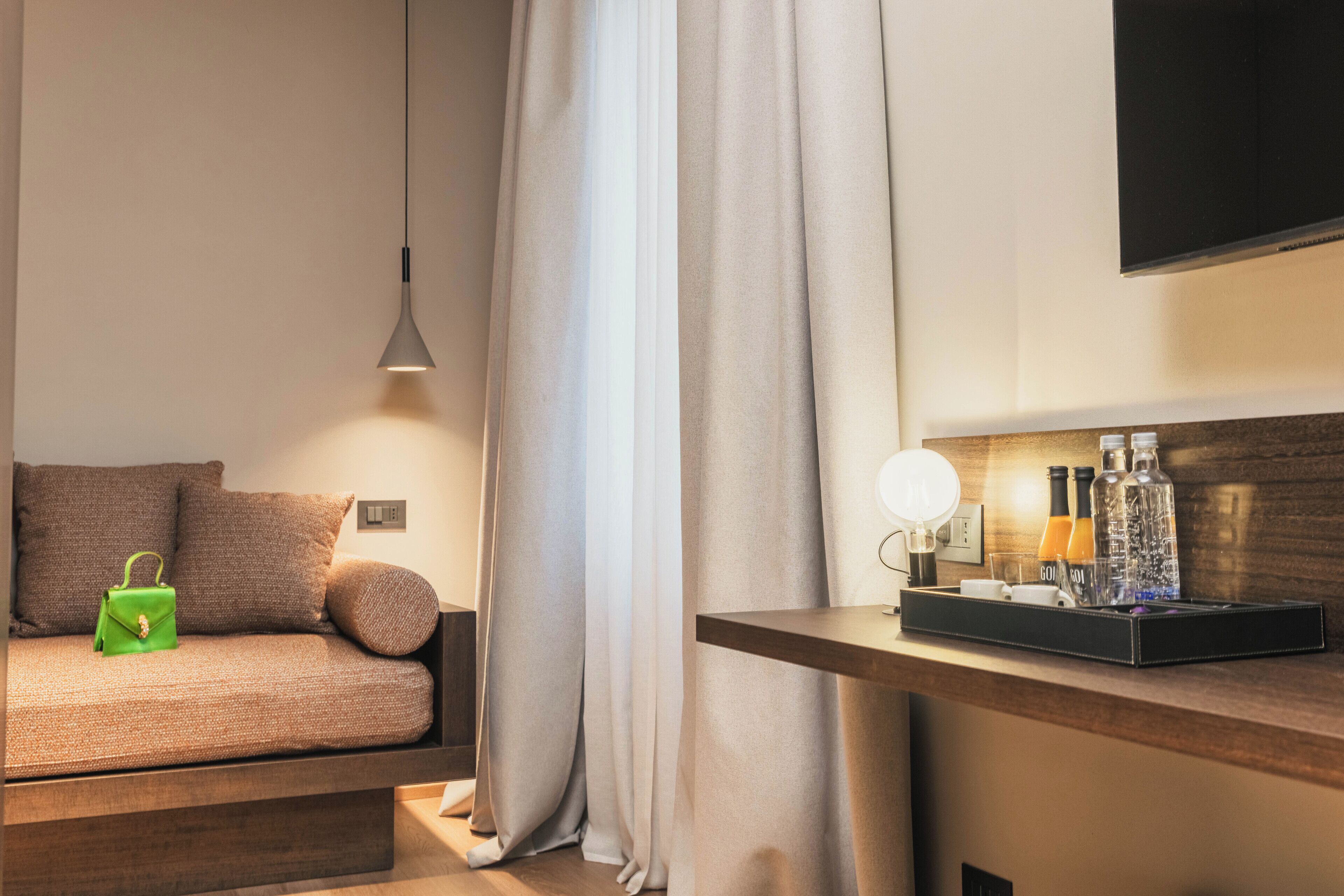 Une chambre d’hôtel moderne, équipée d’un canapé, d’une table de chevet avec une lampe et d’un téléviseur à écran plat fixé au mur.