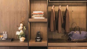 Un armario de madera con ropa colgada, una pila de libros, una cafetera y un florero con flores.