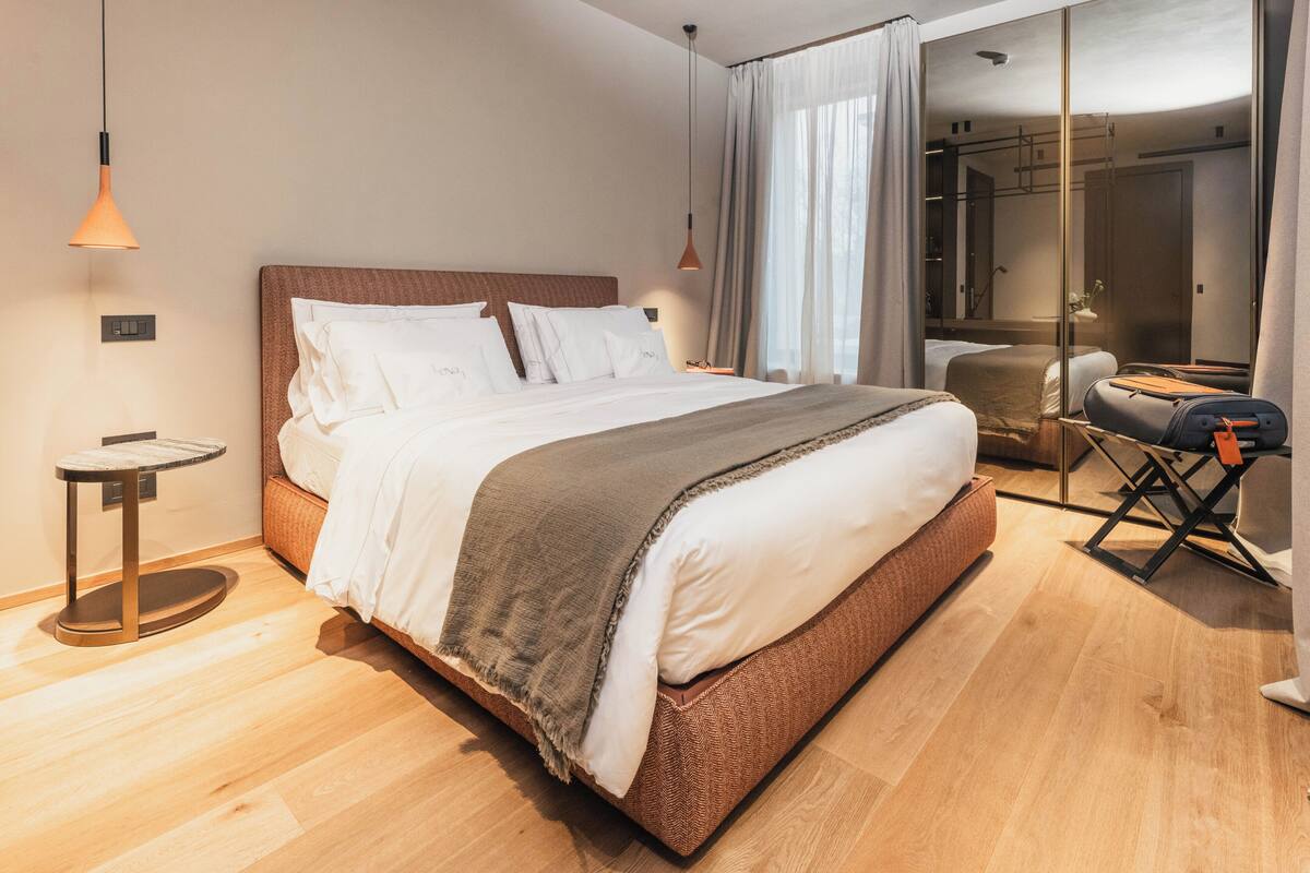 Moderni hotellihuone, jossa on suuri sänky, yöpöydät, peili ja näkymä kaupunkiin.