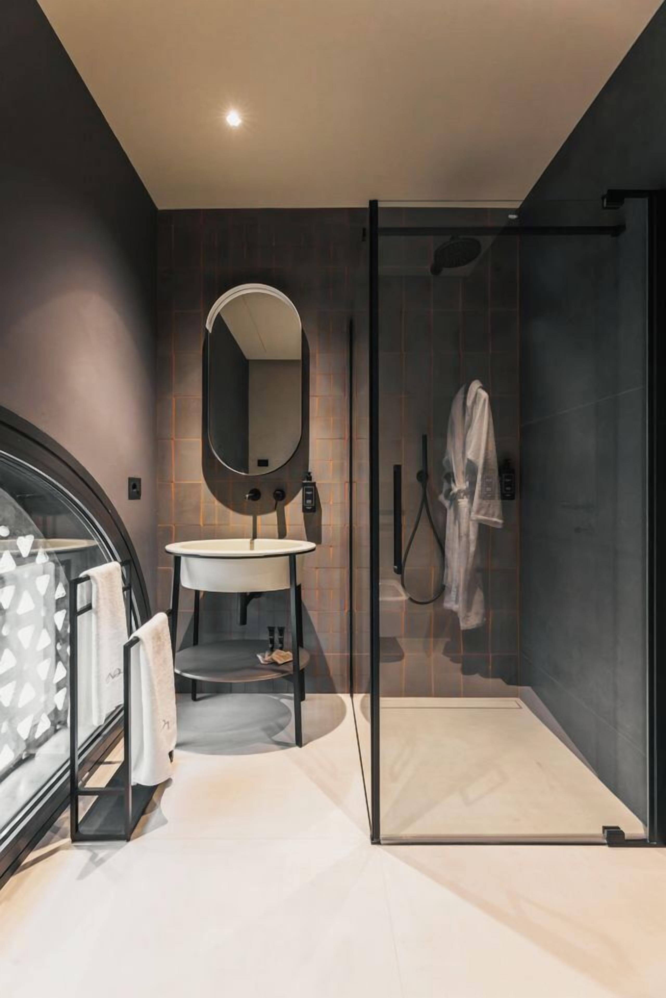 A modern bathroom with a glass shower enclosure, a round mirror, and a vanity with a sink.