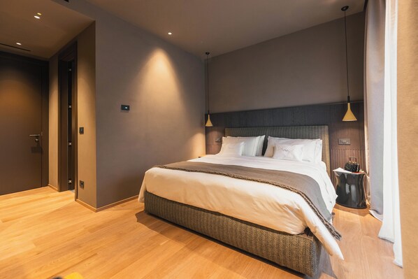 A modern hotel room with a large bed, wooden flooring, and a nightstand with a lamp.