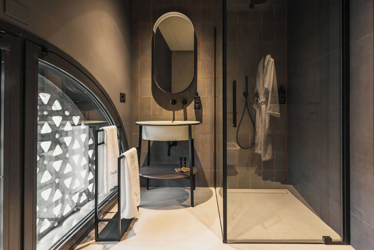 Un bagno moderno con cabina doccia in vetro, uno specchio rotondo, un lavandino e un porta asciugamani.