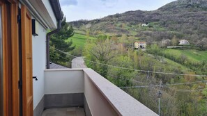 A balcony with a view of a green valley and distant houses.